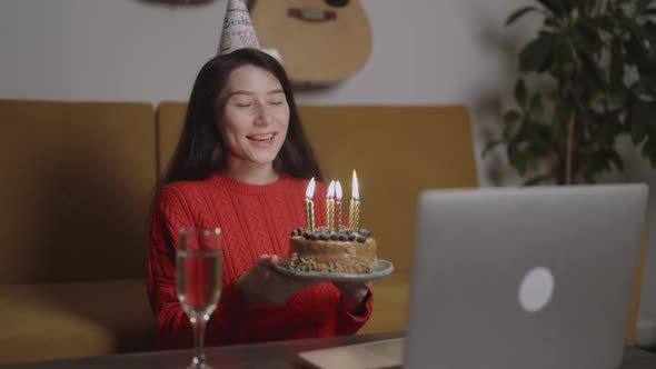 Happy Asian Multiracial Woman in Birthday Cap Celebrating Her Friend Blowing the Candles on Holiday