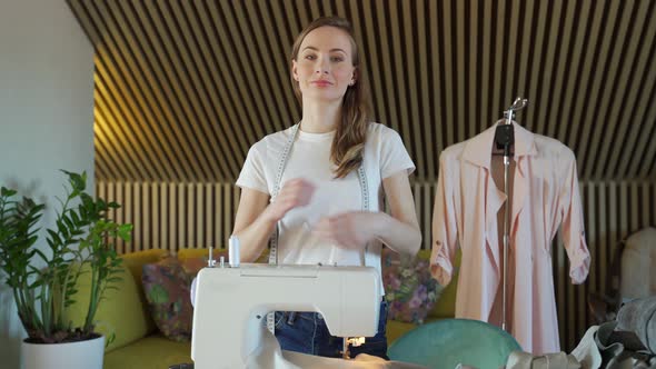 Young Woman Dressmaker Poses in a Workshop Arms Crossed Against the Background of a Sewing Machine