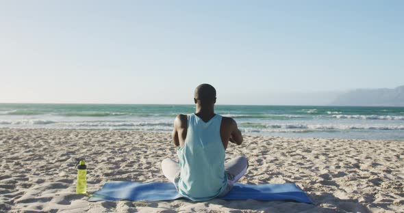 African american man practicing yoga on beach, exercising outdoors by the sea