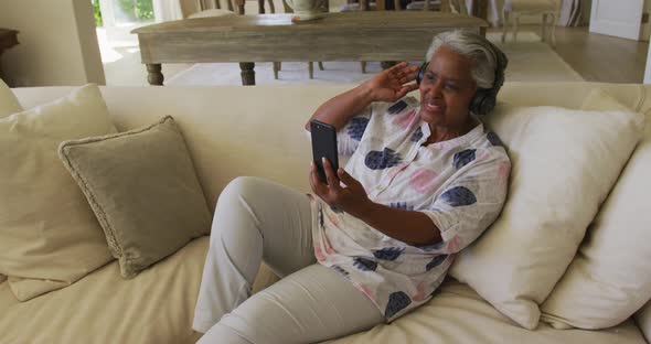 Smiling african american senior woman wearing headphones having a video call on smartphone at home