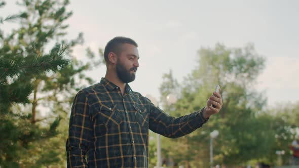 Man in Park Holds His Phone at Arm Length and Talks Someone on Video Call Messenger Side View