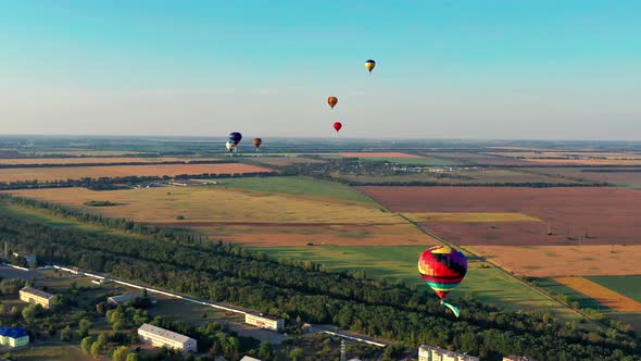 Multicolored balloons fly over fields, houses, trees. Blue sky.