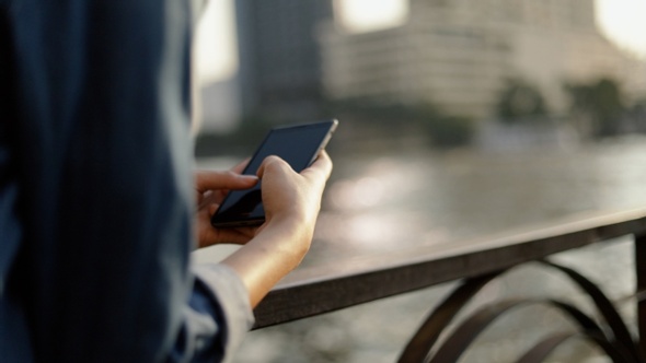 Asian woman using smartphone devices sharing social media while standing beside the river at Bangkok