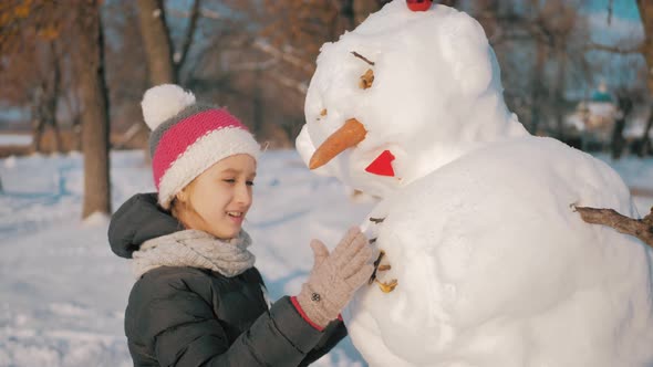 Happy Girl Builds a Snowman in Winter Park