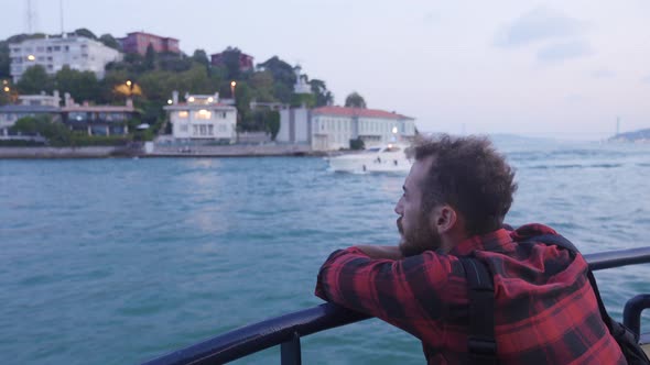 Thoughtful man watching yacht transit on ferry.