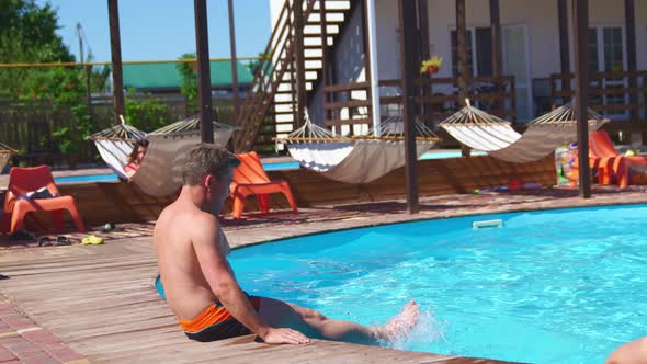 A Man Sits on the Side of the Pool and Chatters His Feet in the Water