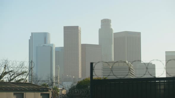 Skyscrapers of Los Angeles seen behind a barb wire sliding gate (daytime) withing traffic in the for