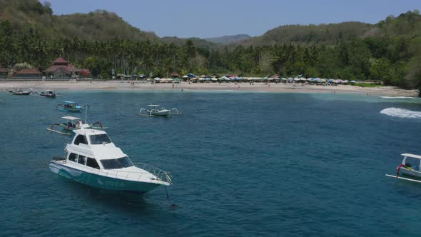 boats anchored in blue tropical ocean near white sand beach in crystal bay nusa penida bali, aerial