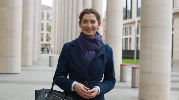 Attractive Happy Businesswoman in Coat Smiling at Camera Near Office Building