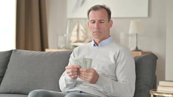 Serious Middle Aged Businessman Counting Dollar at Home