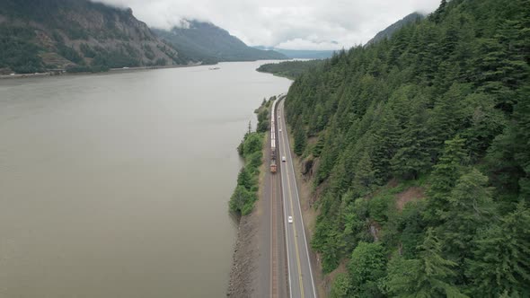 Freight train, traffic along Columbia River travels towards camera, reverse aerial dolly.