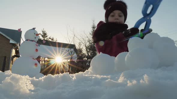 Cute Little Girl Makes Snowballs Near a Funny Snowman