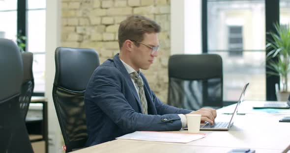 Side View of Exhausted Stressed Caucasian Man in Eyeglasses Working on Laptop. Portrait of Confident