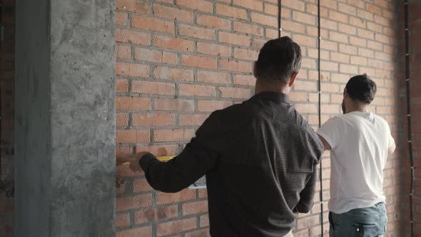 Young and Adult Men Make Wall Measurements in a New Apartment