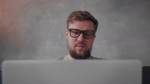 Young Bearded Man with Glasses is Working on a Laptop