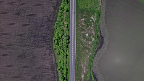 Cars Driving Along the Rustic Asphalt Road Between Fields