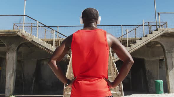 Rear view of african american man with headphones on, standing, taking break in exercise outdoors