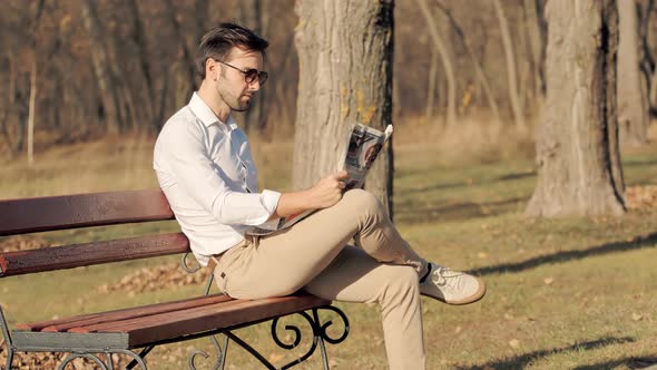 Man Reading Newspaper.Man Sitting On Bench And Reading Newspaper.Man Taking Rest In Park.