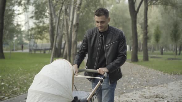 Middle Shot of Smiling Brunette Caucasian Father Strolling with Baby Carriage on Park Alley