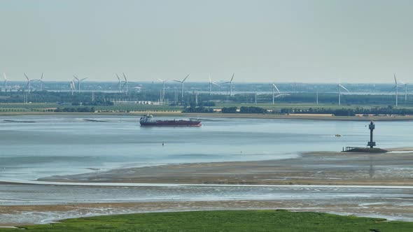 Aerial shot of a cargo ship navigating a river with wetlands on one side and modern industry with wi