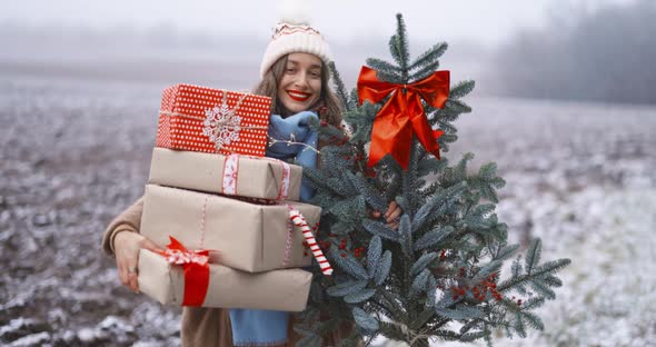 Woman with Gift Boxes and Christmas Branch on the Snowy Field