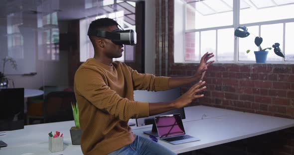 African american businessman sitting on desk using vr headset and gesturing
