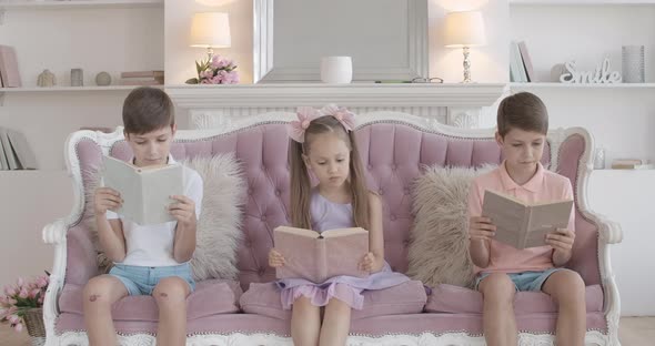 Cute Brunette Girl Sitting on Couch with Twin Brothers and Reading Book, Portrait of Little