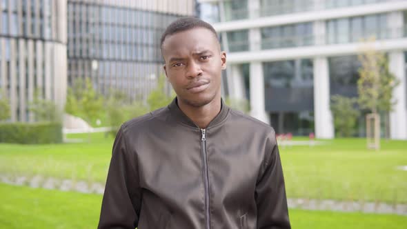 A Young Black Man Shakes His Head at the Camera with a Frown - Office Buildings in the Background