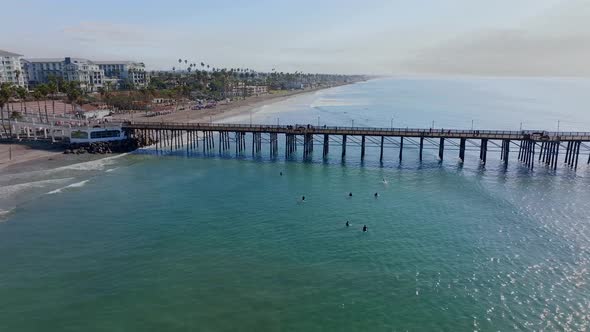 aerial view over Oceanside city coastline. Surfers wait for waves in sea by famous wooden pier