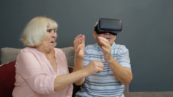 Senior Man Playing Game in Virtual Reality Headset Glasses, Woman Laughing with Him Action at Home