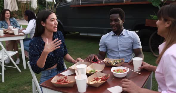 Multiracial friends eating at food truck table outdoor - Summer and lifestyle concept