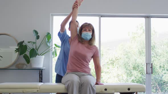 Female health worker stretching arm of senior woman at home