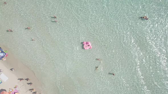 Aerial view of young woman in bikini lie on pink flamingo in azure sea summer beach vacation Italy