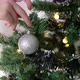 Close-up of woman hands decorating Christmas tree with balls on the background of festive lights - VideoHive Item for Sale