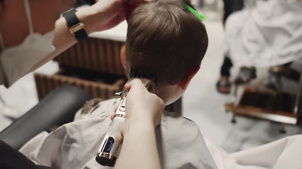 Fashionable Hairdresser Cuts a Child's Hair with a Clipper in a Barbershop