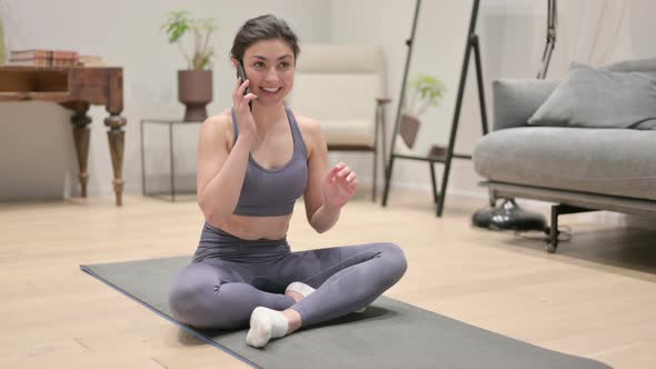 Young Indian Woman Talking on Smartphone on Yoga Mat at Home