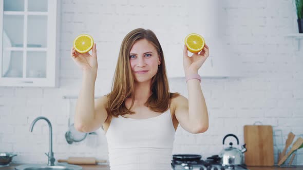 Beautiful woman holding two parts of orange on kitchen background