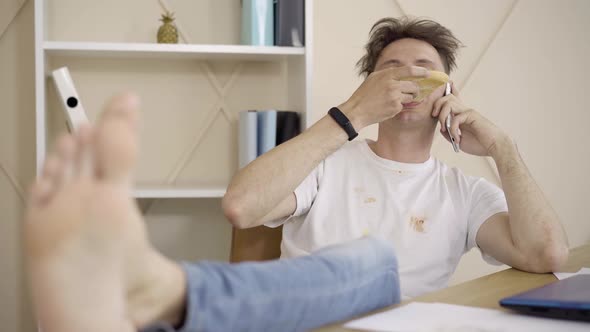 Brunette Young Man with Grey Eyes Eating Pizza and Talking on the Phone