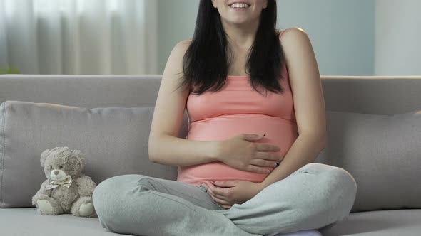 Pregnant Woman Sitting on Couch, Rubbing Stomach and Smiling, Happy Pregnancy