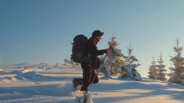 Hiker with Backpack Walking on Snowy Mountain Hillside on Cold Winter Day