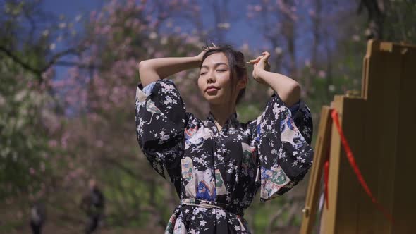 Medium Shot Portrait of Young Creative Japanese Woman in Kimono Making Ponytail Looking at Easel in