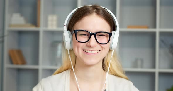 Happy girl student in headphones greets with hand.
