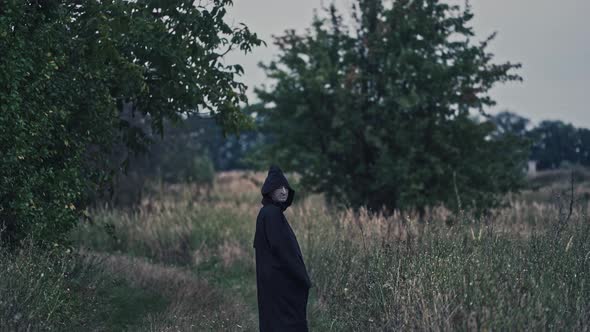 Field with ghost in countryside. Spooky field with ghost in black cloak