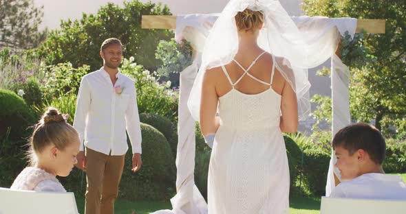 Caucasian bride walking to outdoor altar to groom and wedding officiant