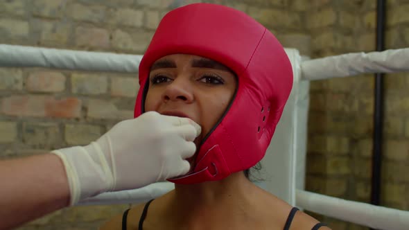 Black Female Fighter in Headgear Inserting Mouthguard with Help of Cutman