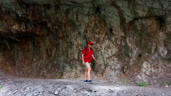 Man hiking in the mountains. Caucasian in red shirt and hat with a backpack walking alone in tunnel