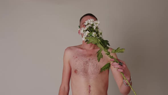 Faceless Shirtless Man in Respirator Smelling Flowers