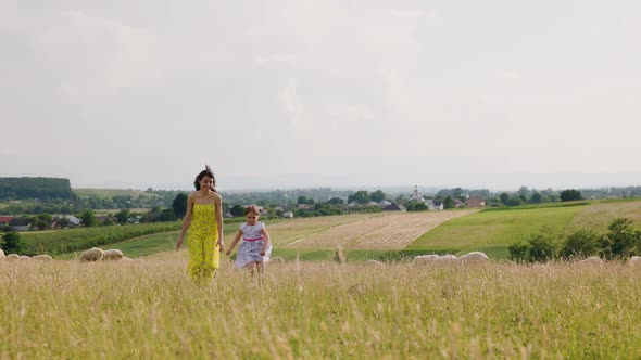 Mother and Doughter Running Near Sheep Lamb Flock at the Grass Field in Summer Day