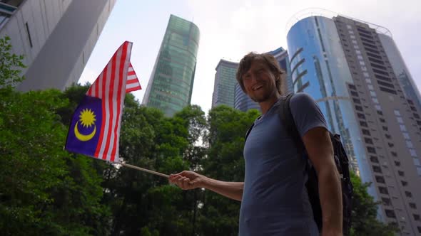 Slowmotion Shot of a Young Man That Holds a Smartphone and Waves Malaysian Flag with Skyscrapers