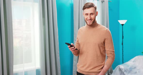 Smiling Millennial Man Stand Using Modern Pad Gadget at New Home Browsing Internet or Shopping